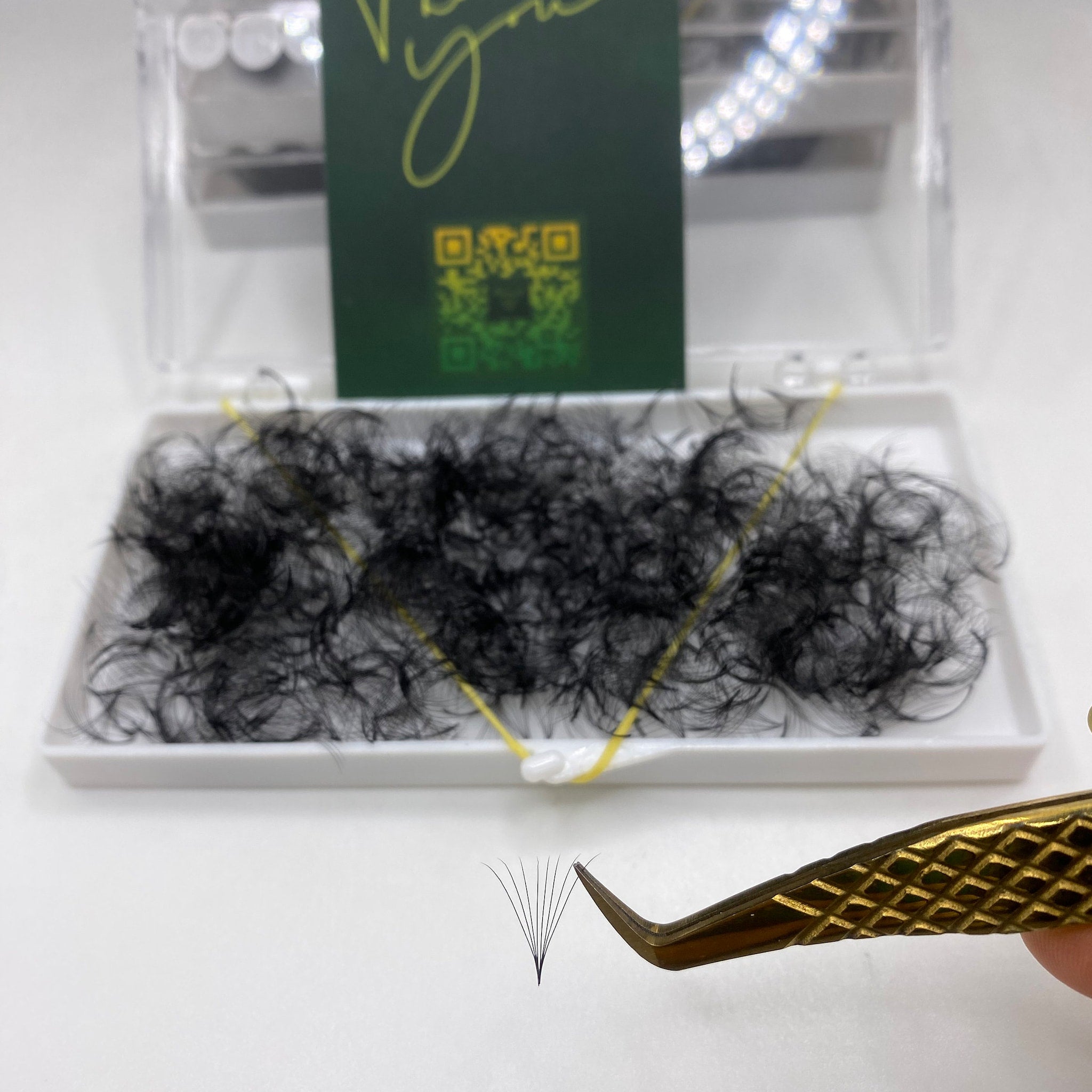 Eyelash extensions in black, with gold tweezers, and white tray for application