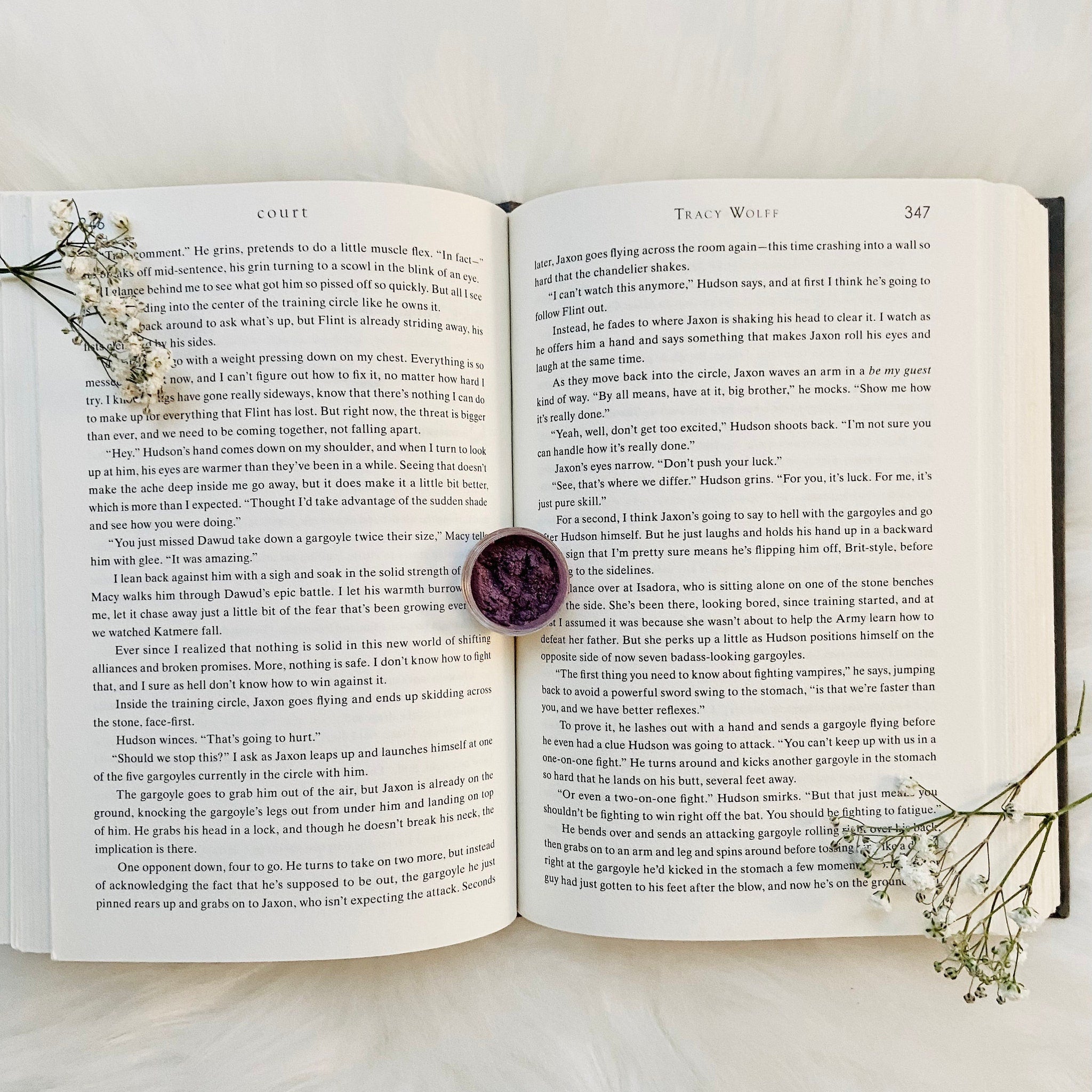 Eye shadow pot with purple, textured, round compact on open book pages