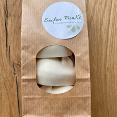 Soap bars in white, visible through brown paper bag with Seifen Punkt label on wood background