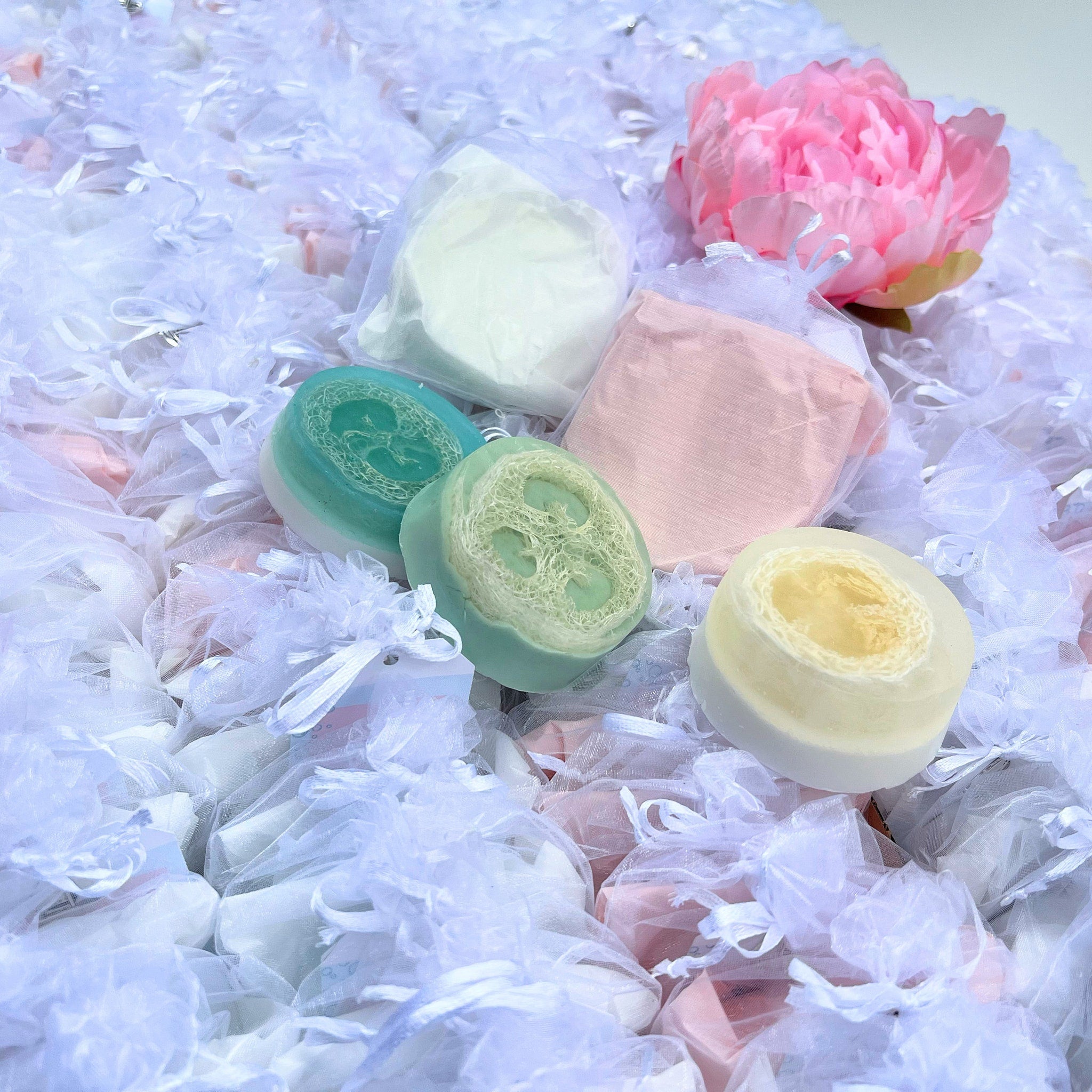 Soap bars with loofah, green and yellow round, surrounded by white tulle bags and pink flower
