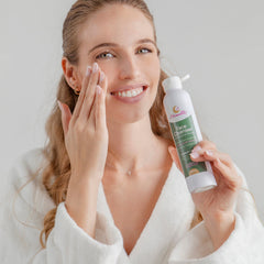 Facial cleanser bottle, white and green label, held by woman applying to face Moonette