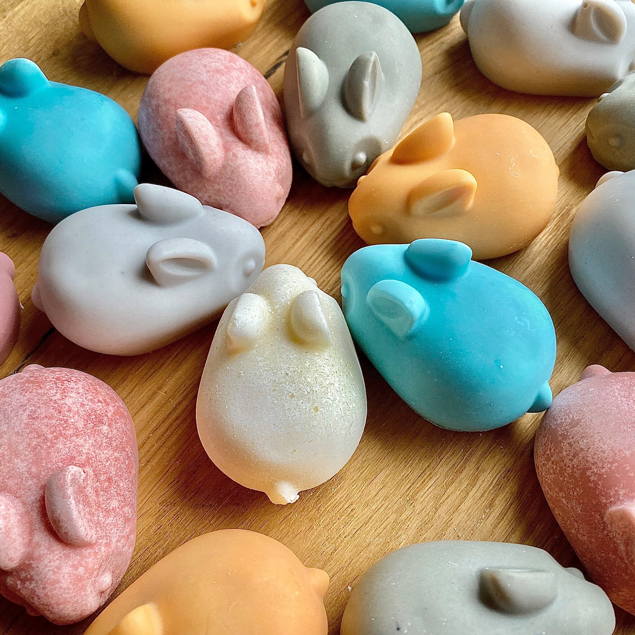 Bunny shaped soaps in various colors, smooth and speckled texture, on wooden surface