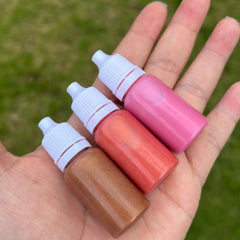 Lip gloss bottles, pink, red, and bronze metallic colors, held in hand