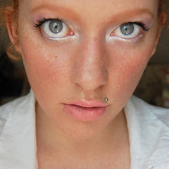 Face with freckles, light skin, gray eyes, and lip piercing, wearing white shirt