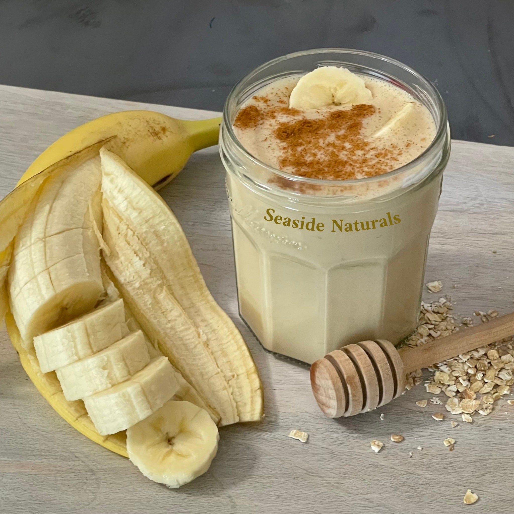 Banana smoothie in clear glass with cinnamon, sliced banana, and Seaside Naturals text on glass