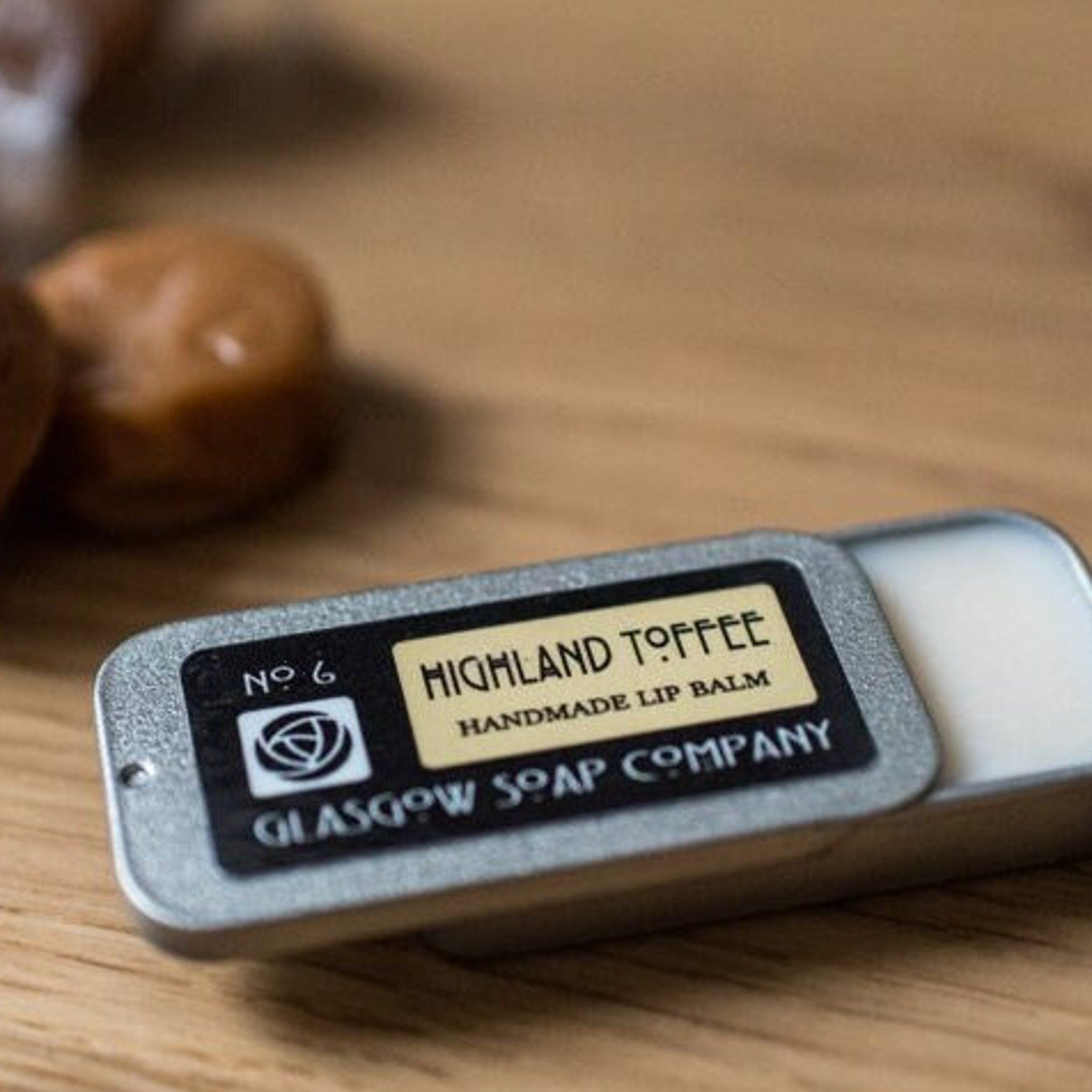 Lip balm in silver tin with black label and Highland Toffee text on wooden surface