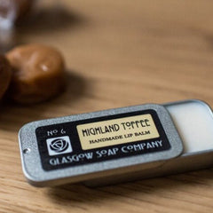 Lip balm in silver tin with black label and Highland Toffee text on wooden surface
