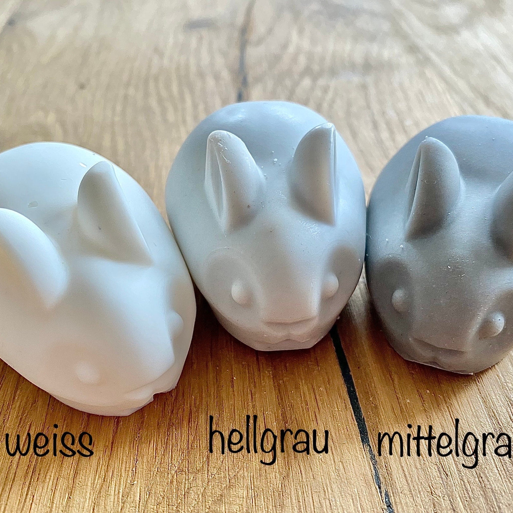 Rabbit figurines in white, light gray, and medium gray colors, on a wooden surface