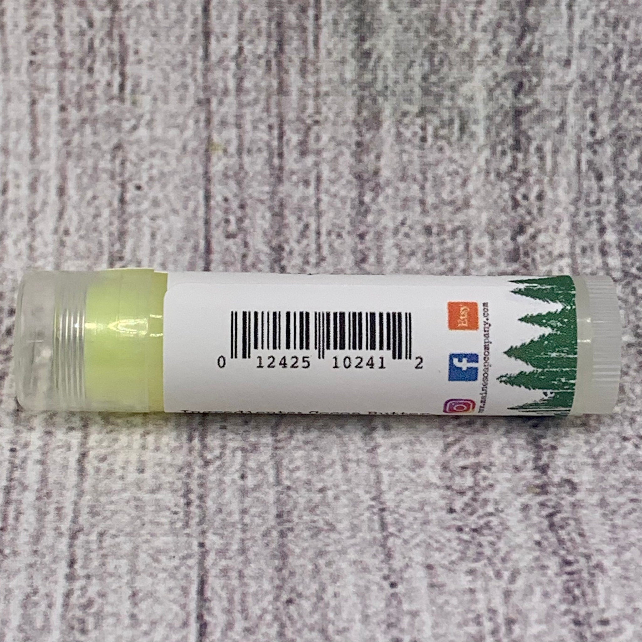 Lip balm tube with green balm, white label, and clear plastic casing on wood background