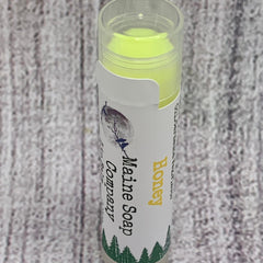 Lip balm tube with yellow balm, white label, and Maine Soap Company text on wood background