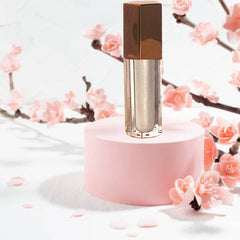 Lip gloss with gold cap, clear tube, and silver shimmer, on pink display