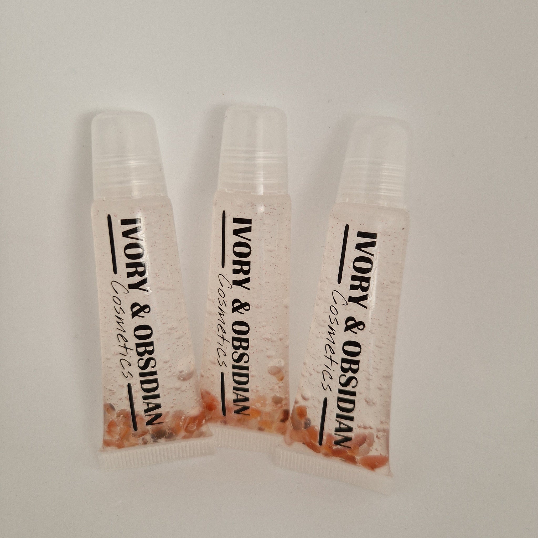Lip gloss tubes with clear plastic, pink liquid, and Ivory & Obsidian Cosmetics text