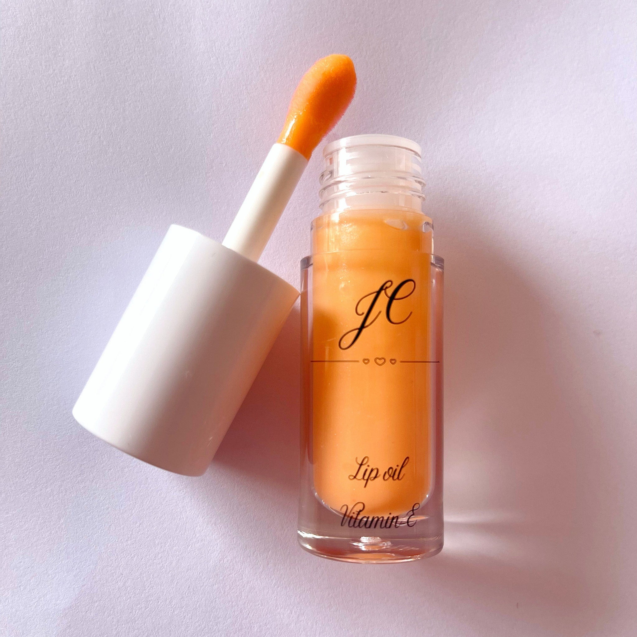 Lip oil with orange liquid, white applicator, and clear glass bottle with text