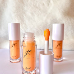 Lip oil bottles with orange liquid, white caps, and JC text, Vitamin E label visible