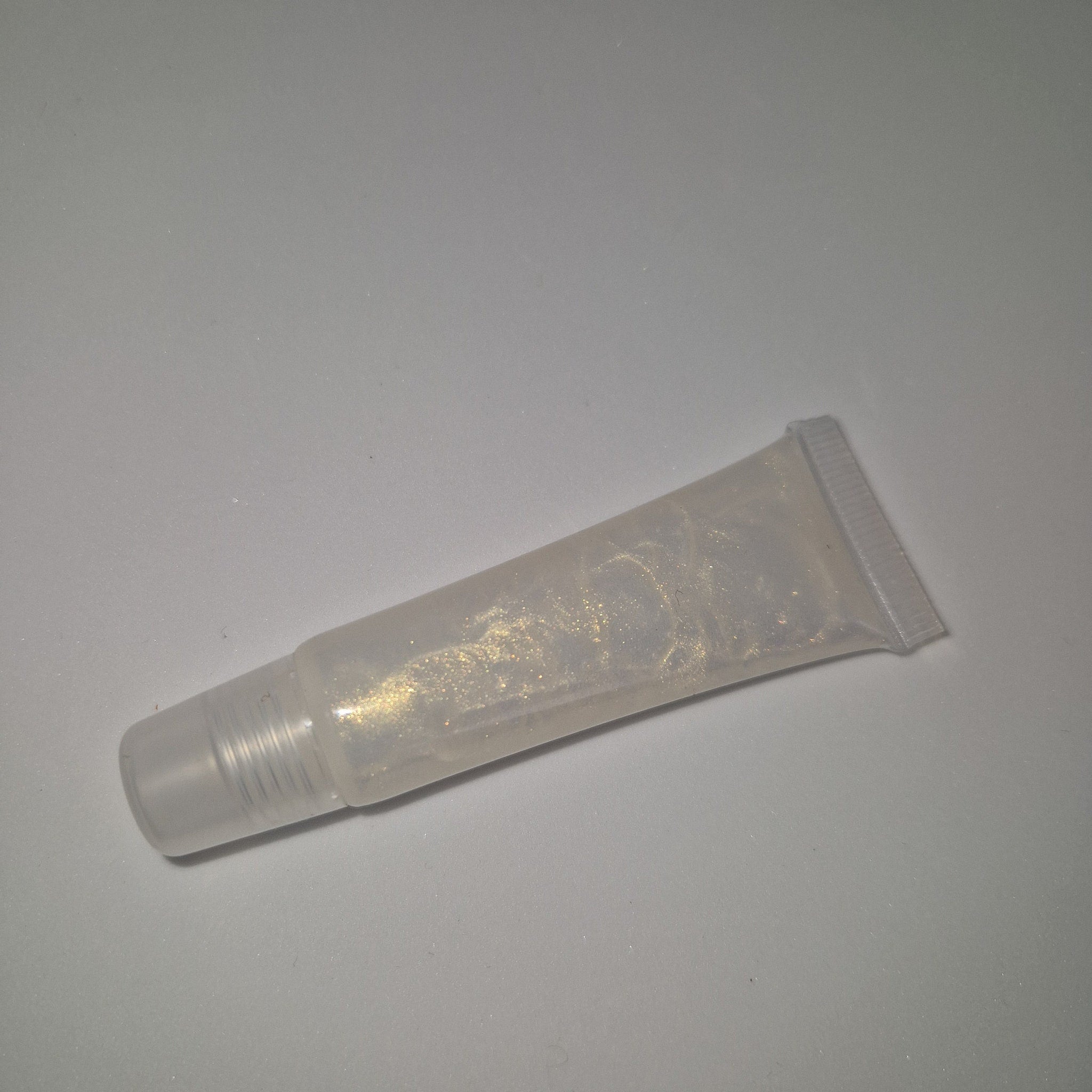 Lip gloss tube with clear plastic, gold shimmer, and angled tip