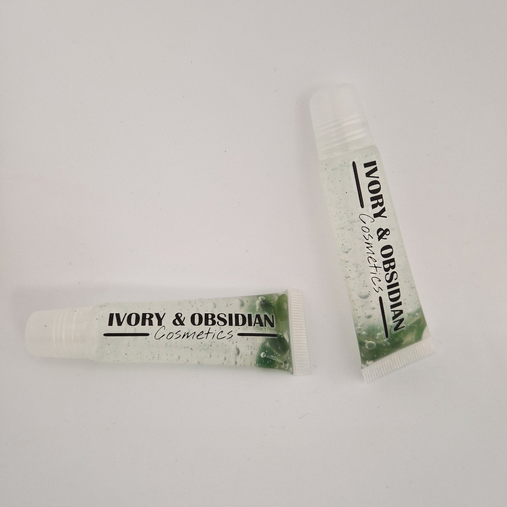 Lip gloss tubes with clear liquid, green beads, and "IVORY & OBSIDIAN Cosmetics" text on white background