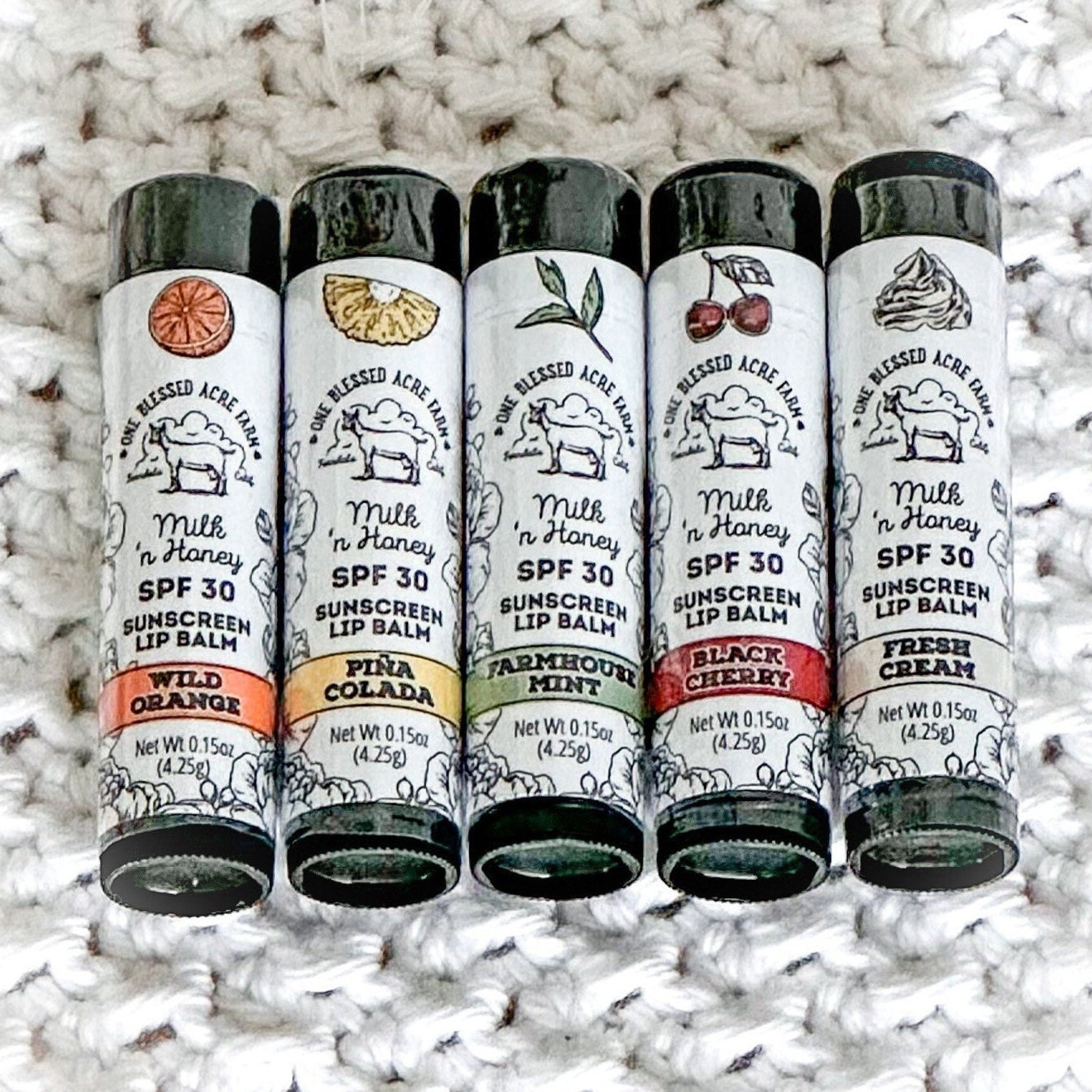 Lip balm tubes with black caps, white labels, and colorful flavor bands, One Blessed Acre Farm brand