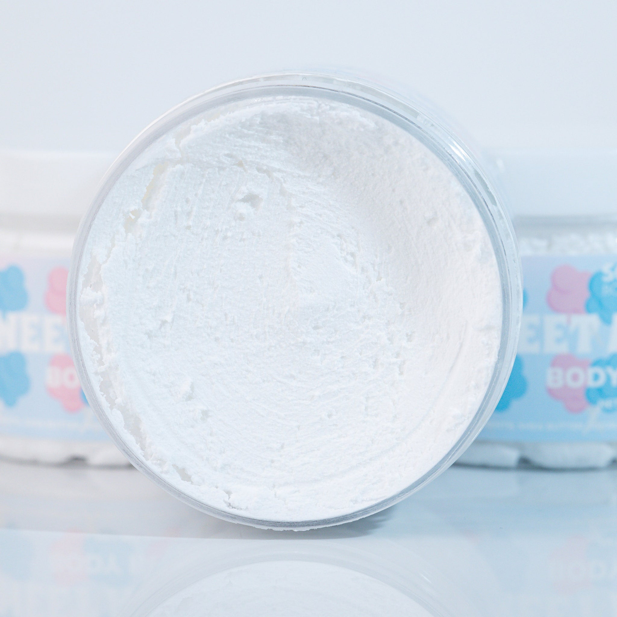 White cream in clear plastic jar, textured surface, Soogs Body Care visible in background