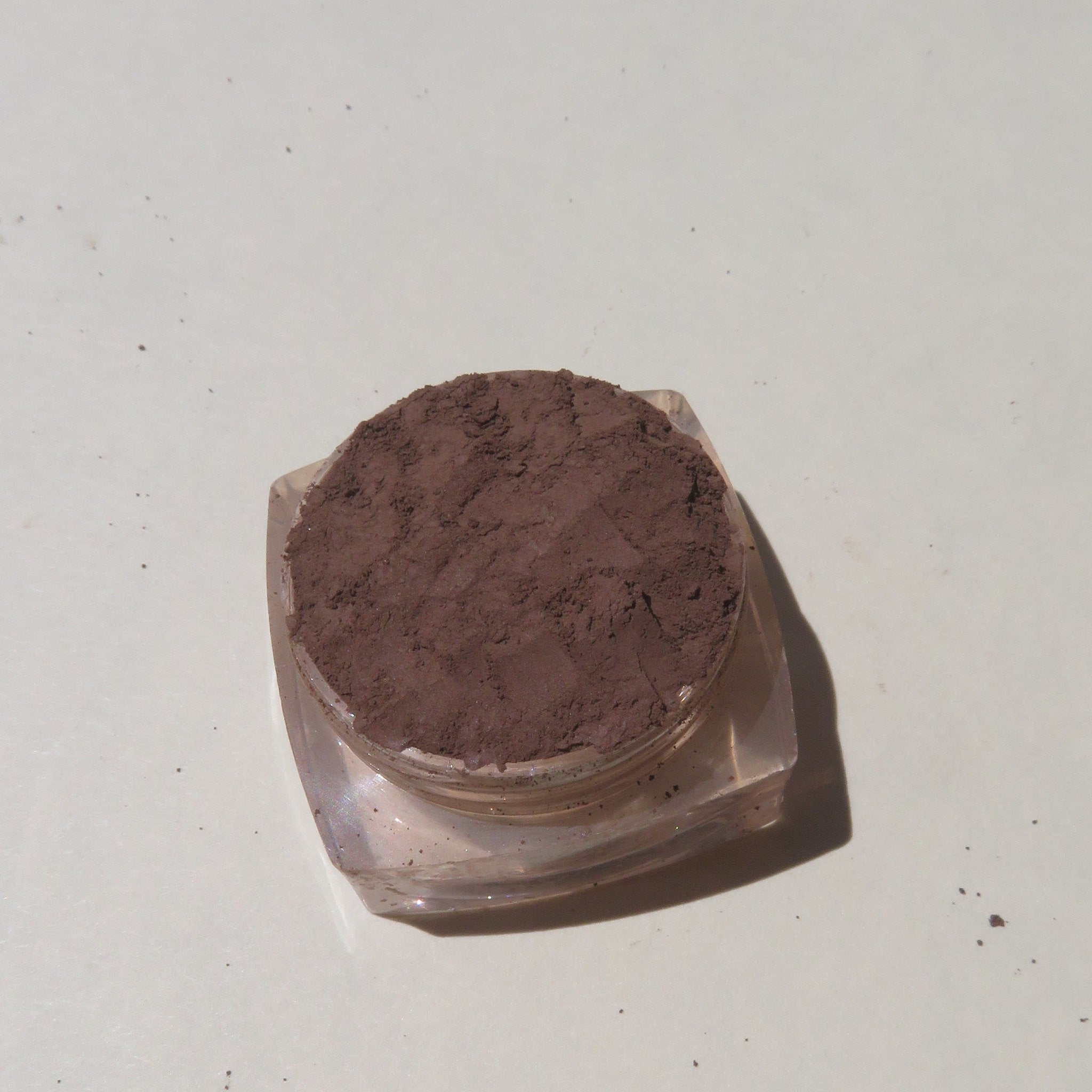 Hand applying matte dark brown mineral eyeshadow with a brush, showcasing loose powder pigment blending on eyelid.