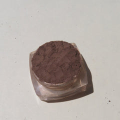 Hand applying matte dark brown mineral eyeshadow with a brush, showcasing loose powder pigment blending on eyelid.