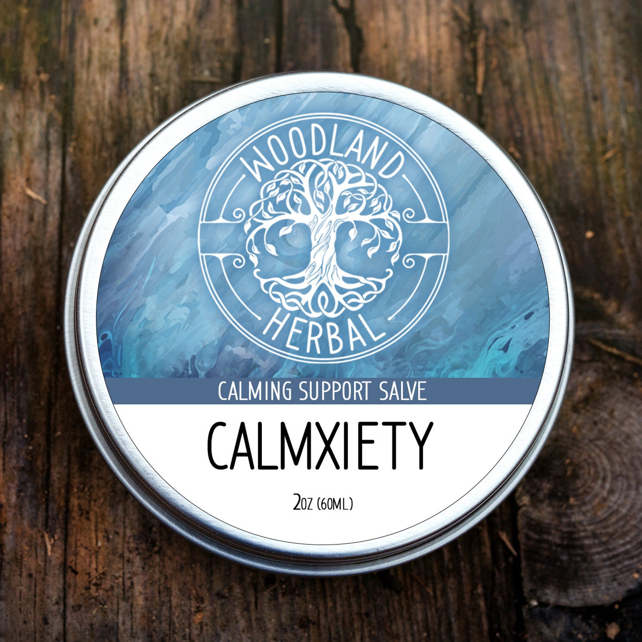 Calming salve tin with blue watercolor pattern, white text, and silver rim on wood surface
