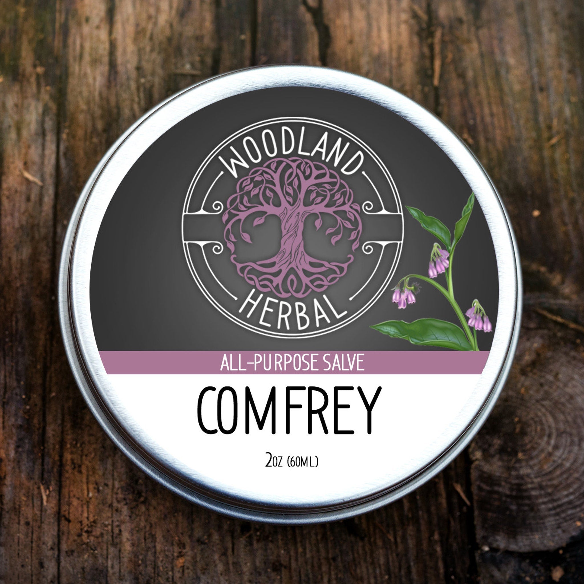 Comfrey salve tin with silver rim, black and purple label, and Woodland Herbal text