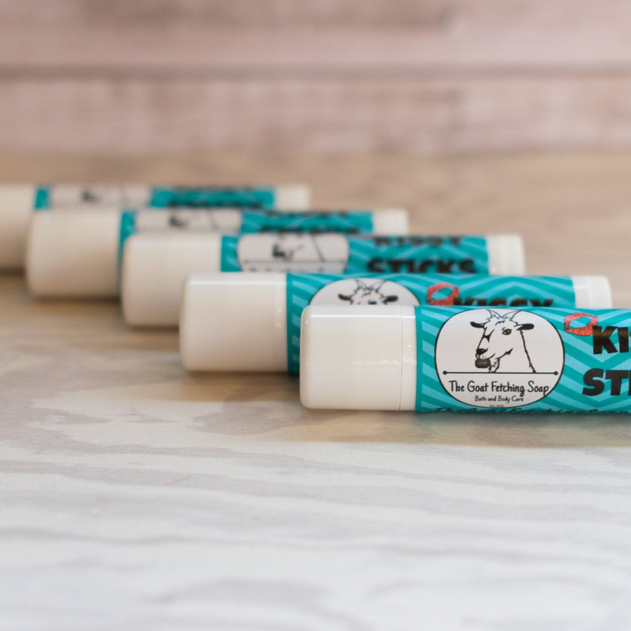 Lip balm sticks with white tubes, teal chevron pattern, and The Goat Fetching Soap logo