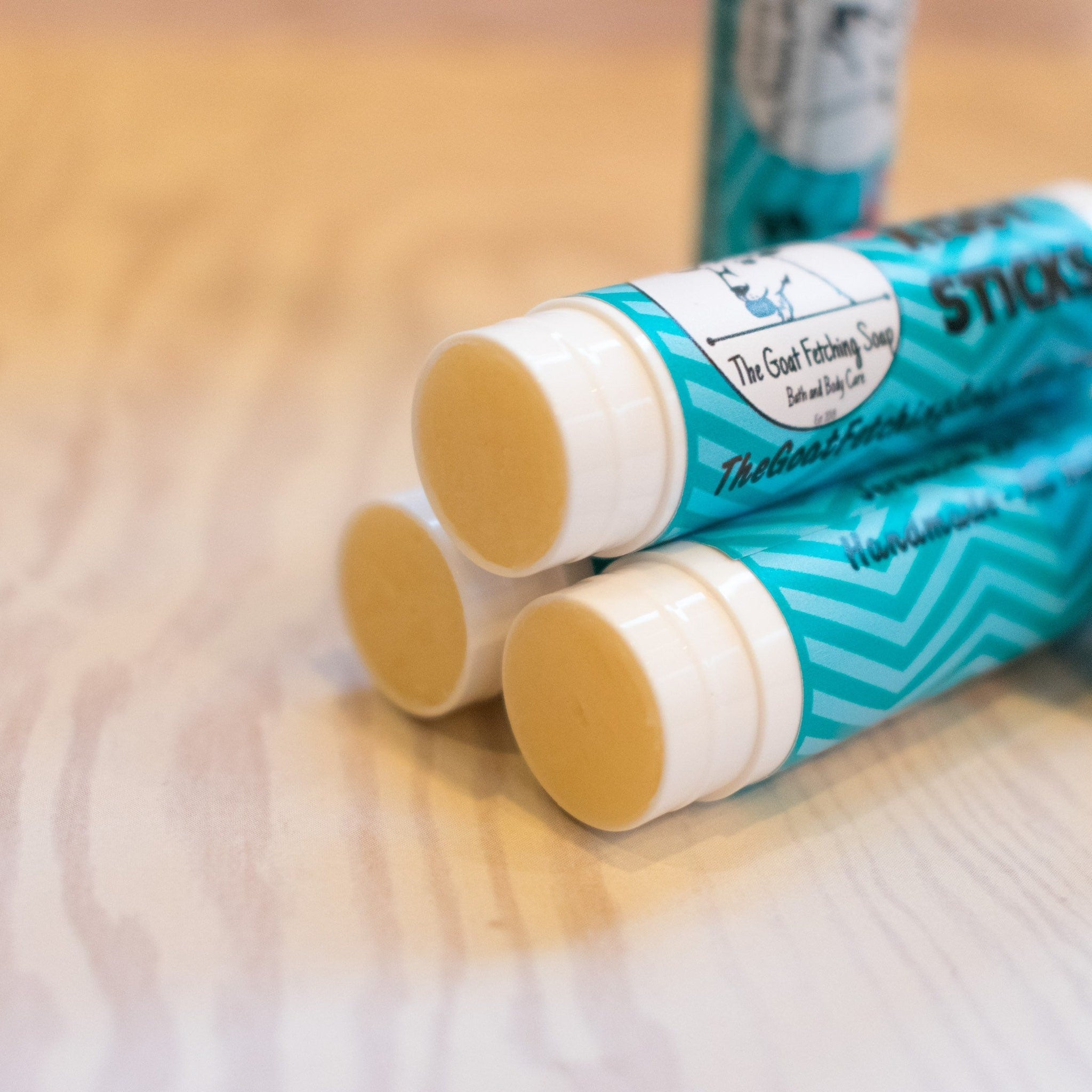 Lip balm sticks, white and teal tubes with chevron pattern, The Goat Fetching Soap brand visible