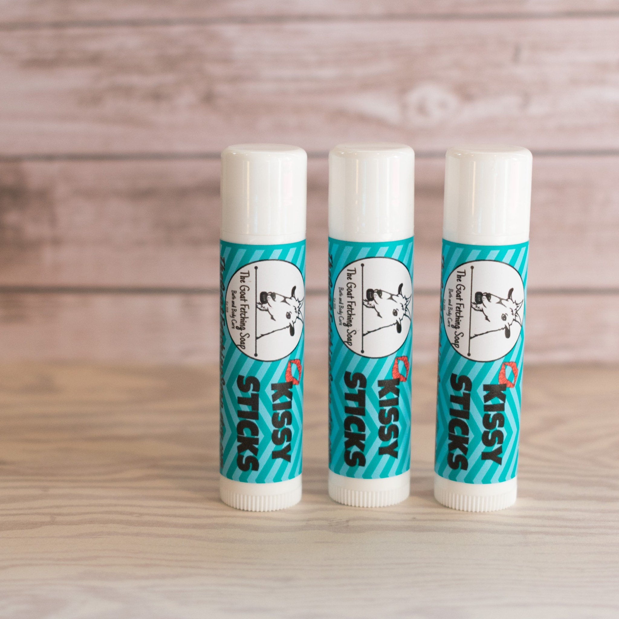 Lip balm tubes with white caps, teal and white striped label, and brand name "Kissy Sticks