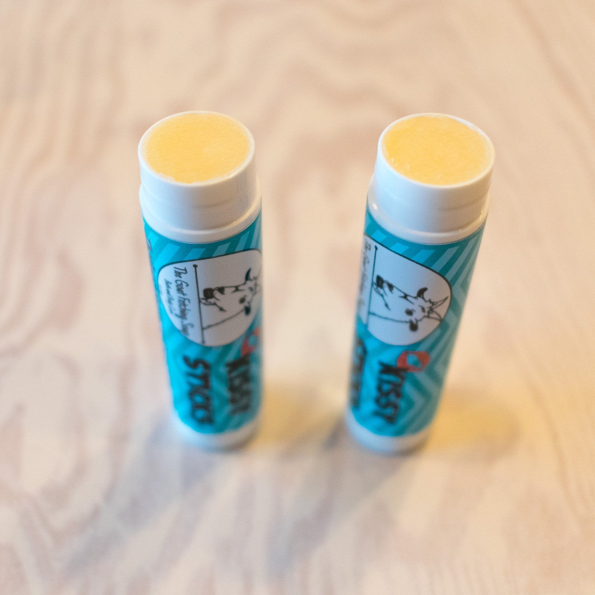 Lip balm sticks with white and teal packaging, yellow balm, and The Goat Fetching Soap brand text