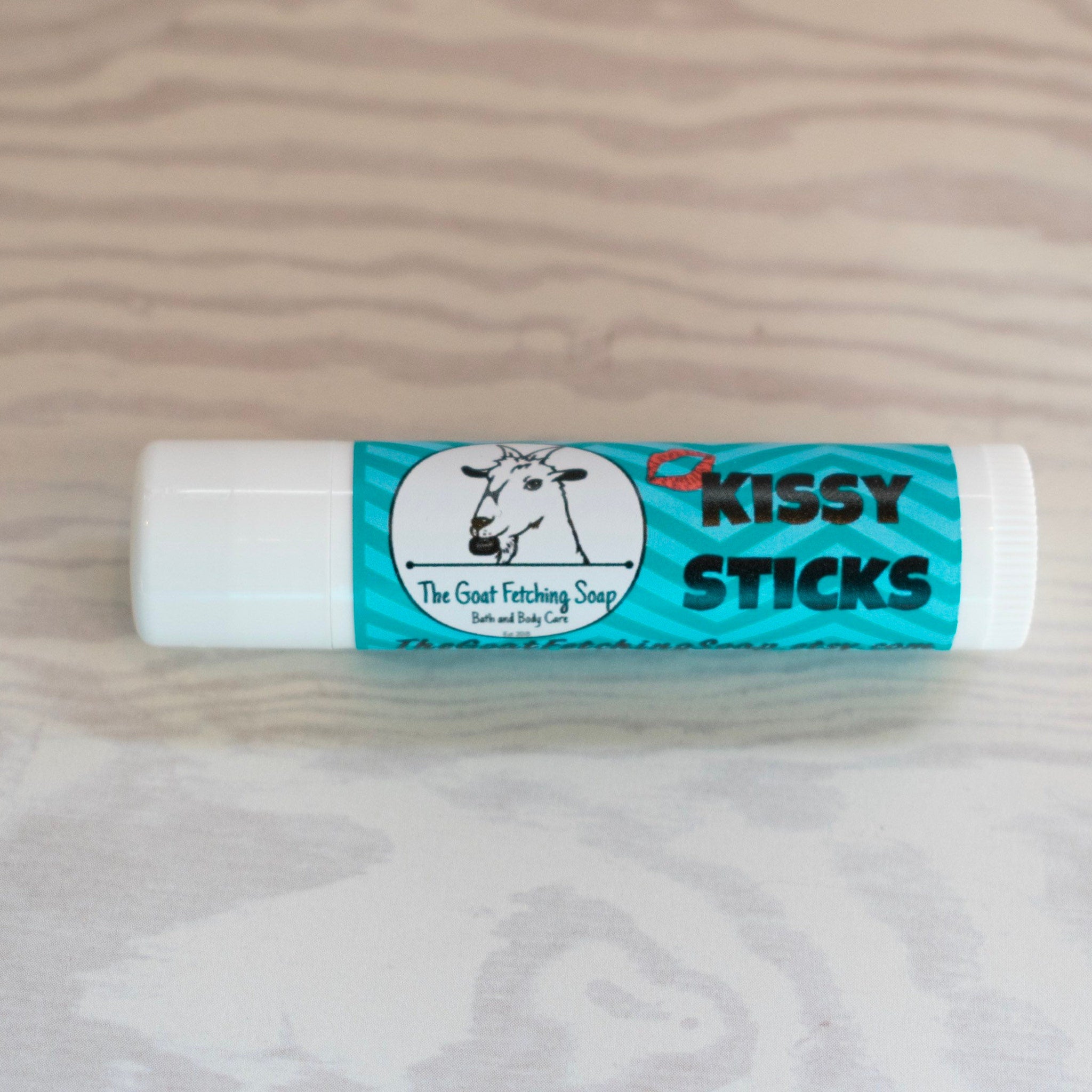Lip balm tube with white and teal label, "Kissy Sticks" text, and The Goat Fetching Soap brand