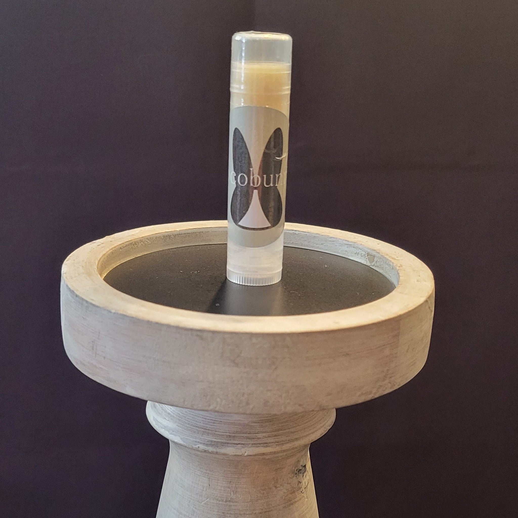 Lip balm tube with clear plastic, "cobun" label, and light-colored balm on a wooden stand with dark top