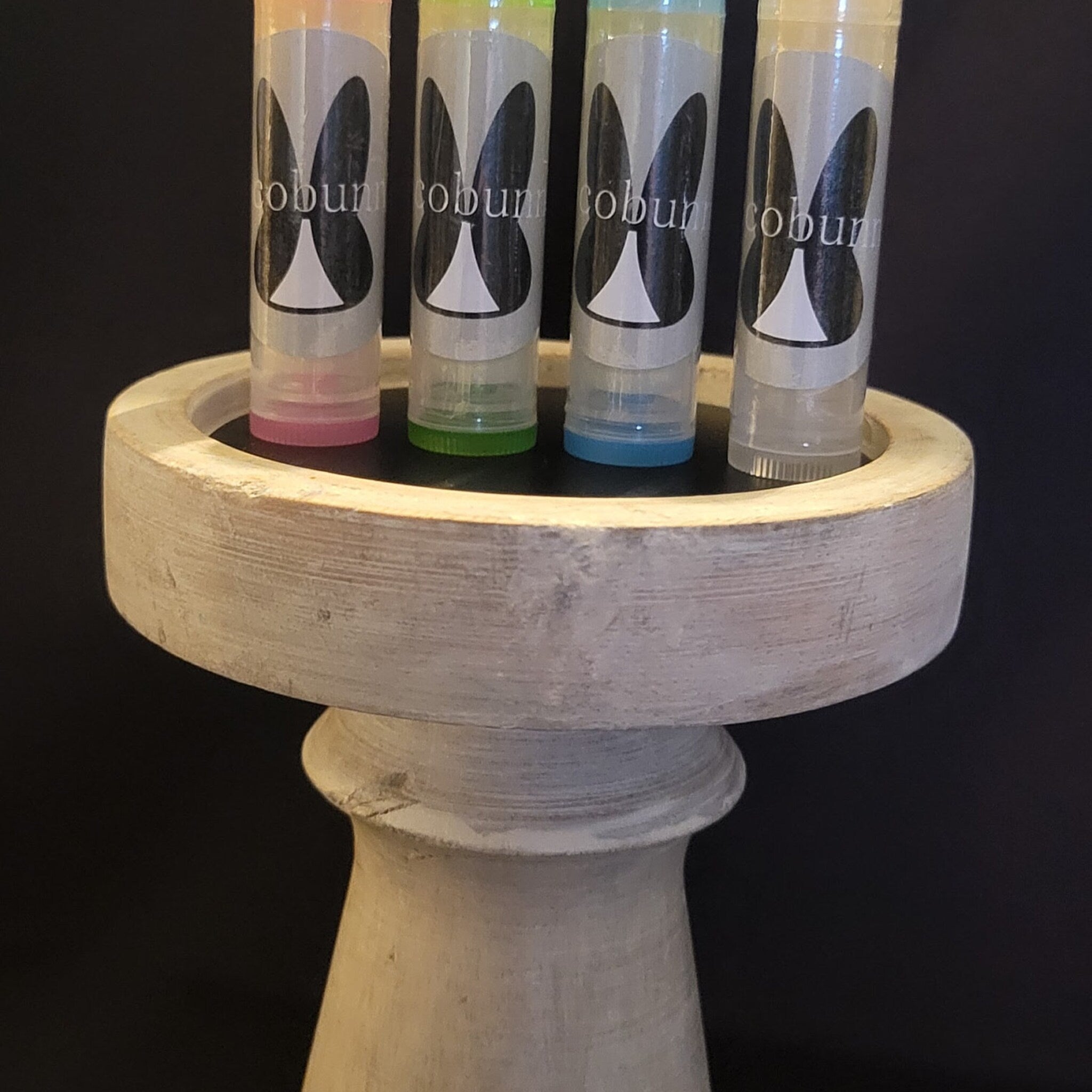 Lip balm tubes with colorful bases and "cobunn" logo, displayed on a wooden stand
