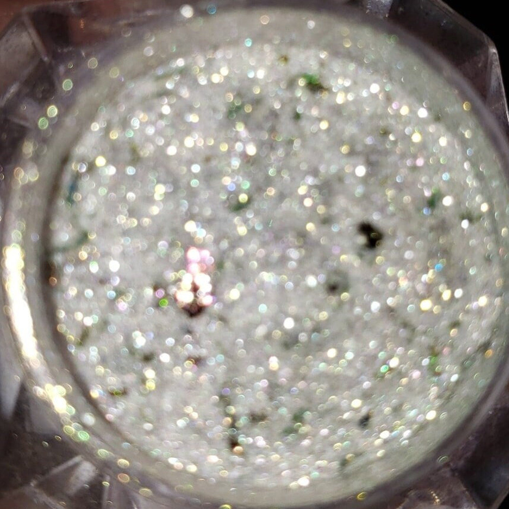 Close-up of shimmering loose glitter eye shadow in a small jar with metallic lid, showcasing vibrant sparkles