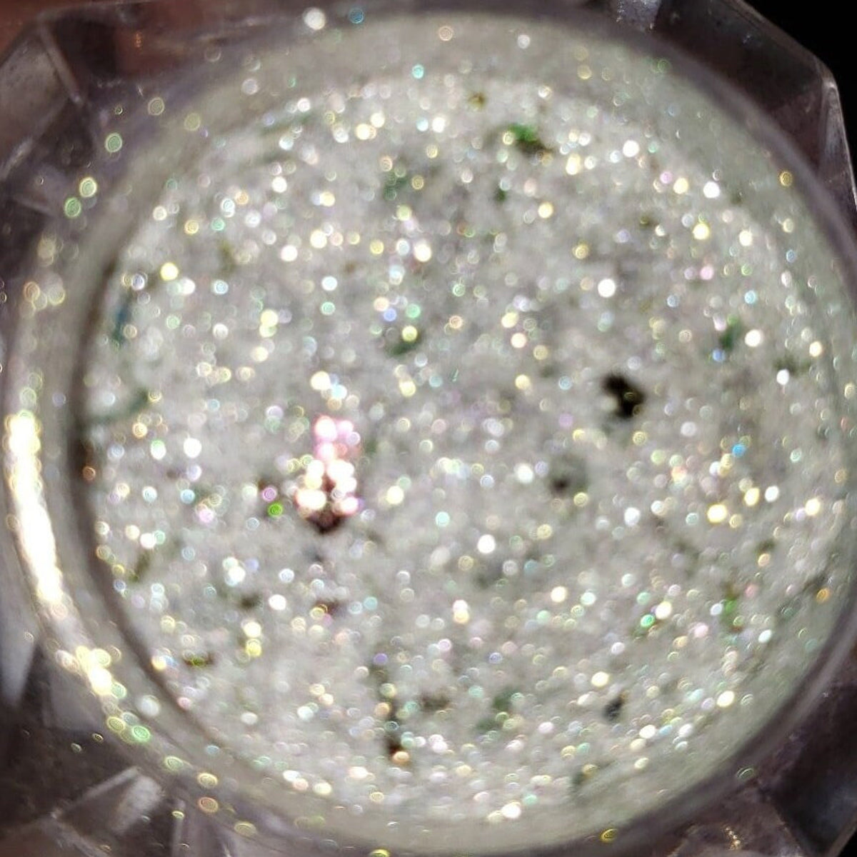 Close-up of shimmering loose glitter eye shadow in a small jar with metallic lid, showcasing vibrant sparkles