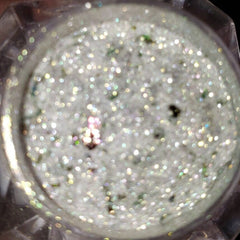Close-up of shimmering loose glitter eye shadow in a small jar with metallic lid, showcasing vibrant sparkles