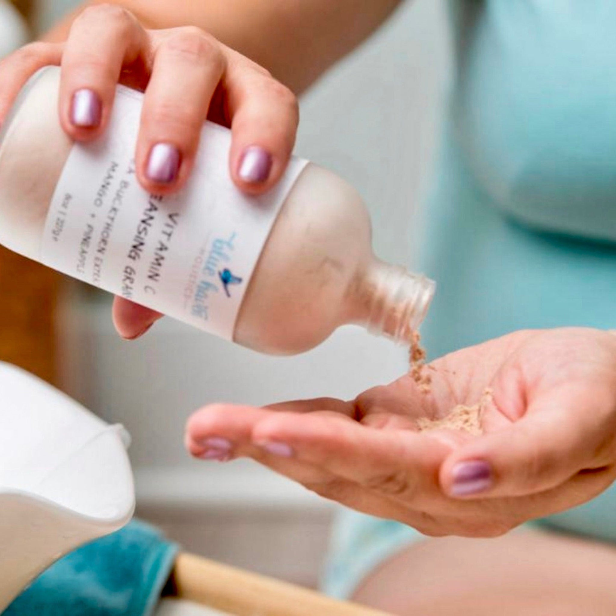 Vitamin C cleansing granules, white bottle with blue logo, pouring into hand