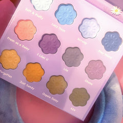 Eyeshadow palette with flower-shaped pans in various colors on a lavender background, names visible