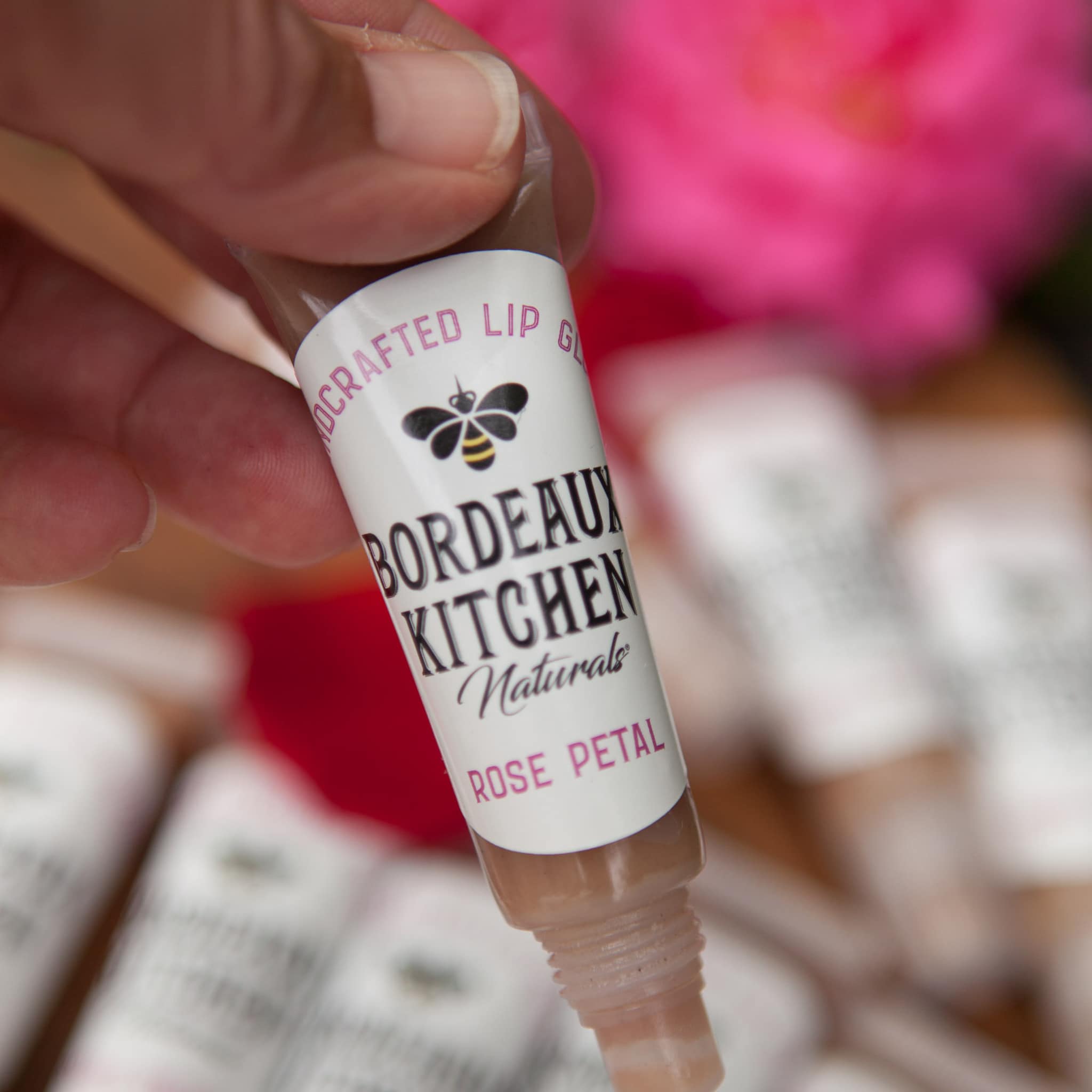 Lip gloss tube with clear plastic, beige gloss, and Bordeaux Kitchen Naturals label held by hand.