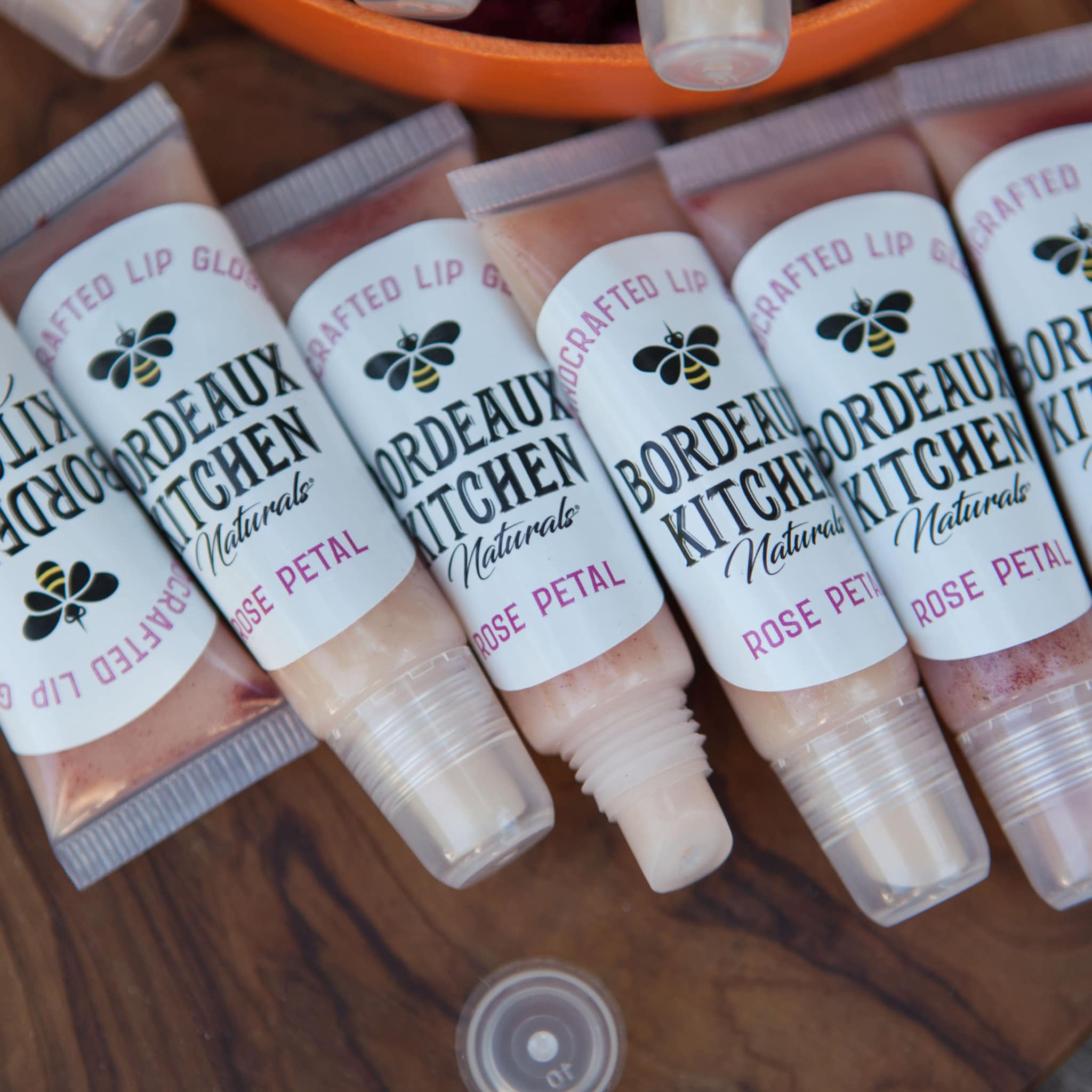 Lip gloss tubes with clear plastic, pink liquid, and white labels with "Bordeaux Kitchen" text