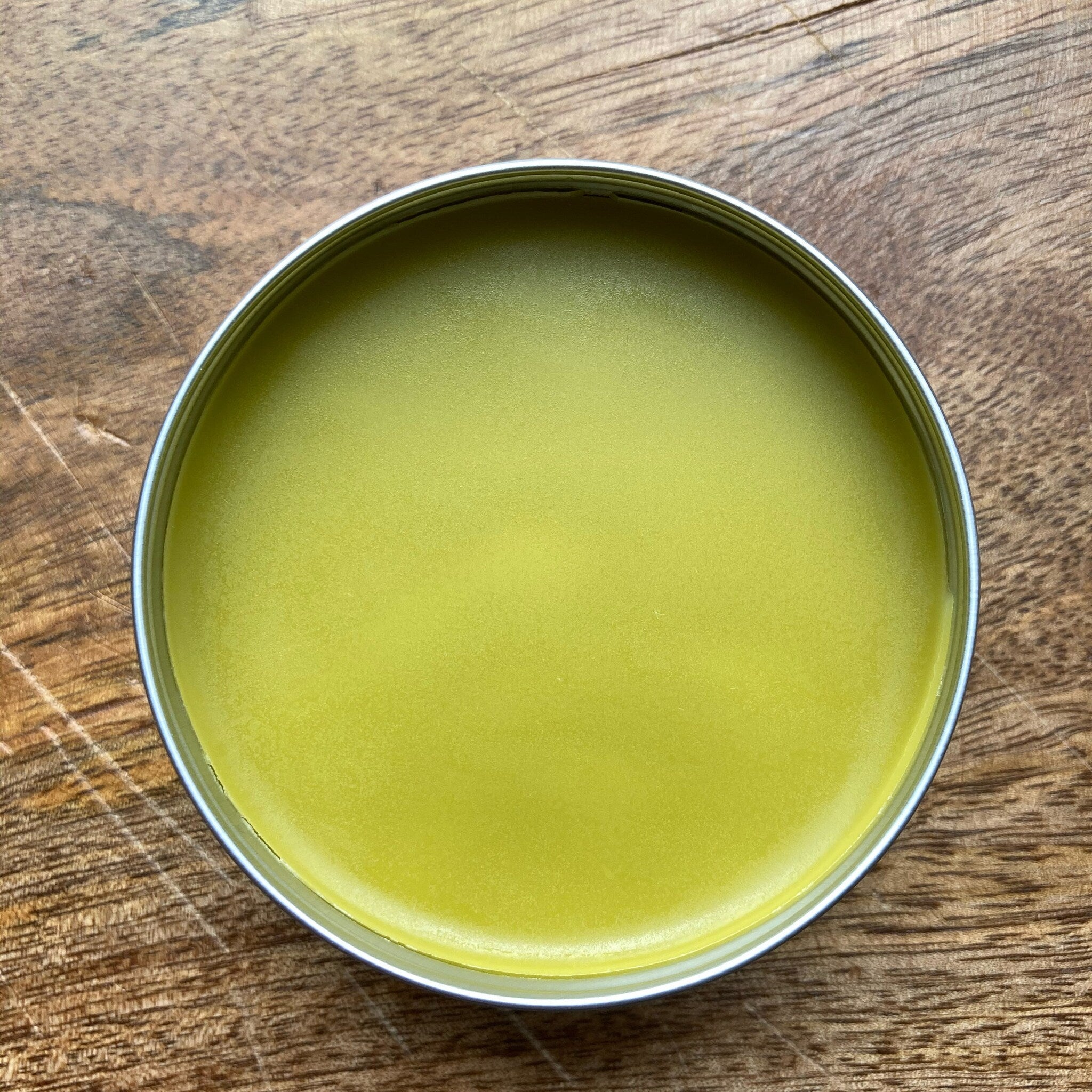 Yellow balm in a silver tin on a wooden surface, top-down view