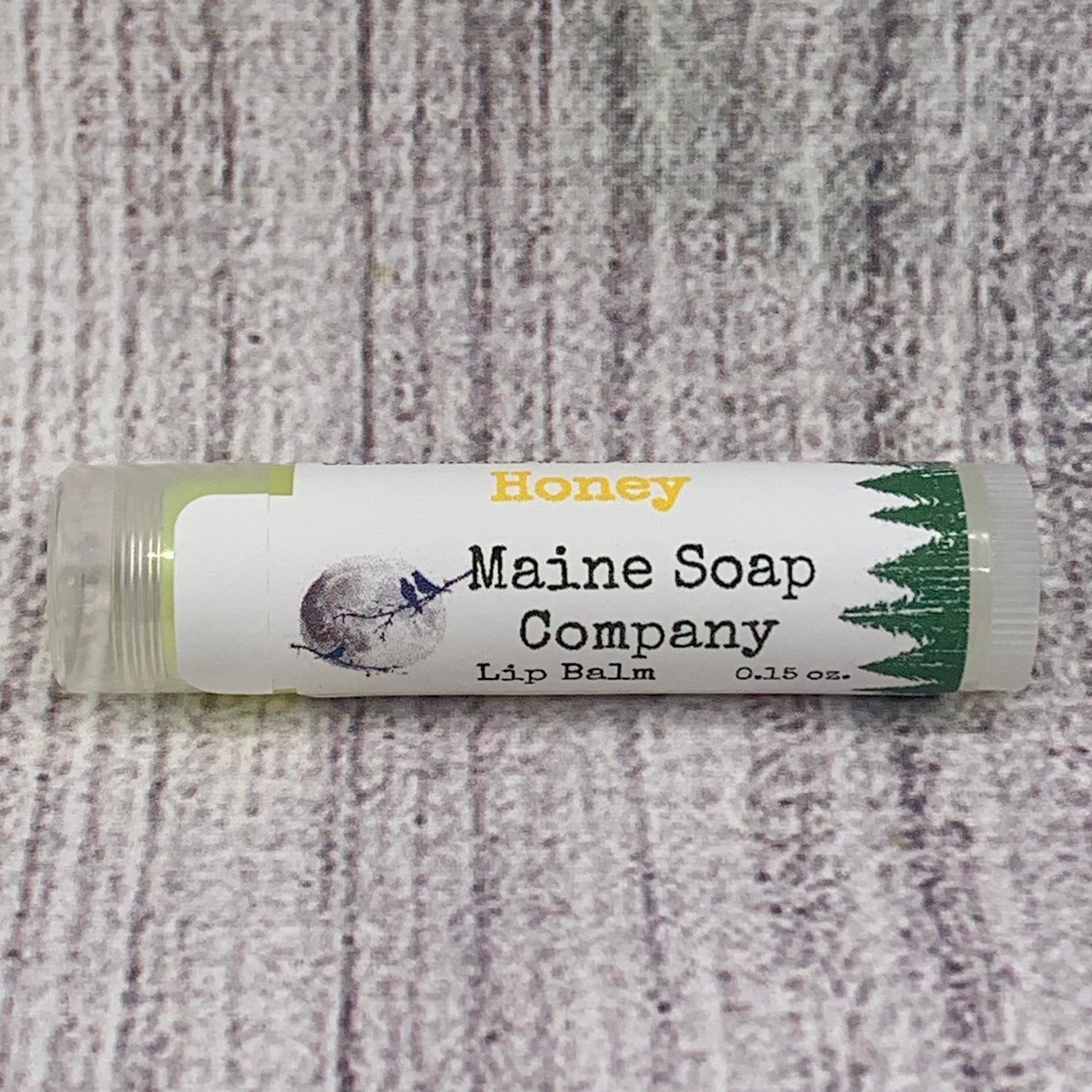 Lip balm tube with white label, green and yellow text, and clear plastic casing