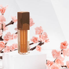 Lip gloss tube with metallic gold cap and bronze shimmer, displayed on a white surface