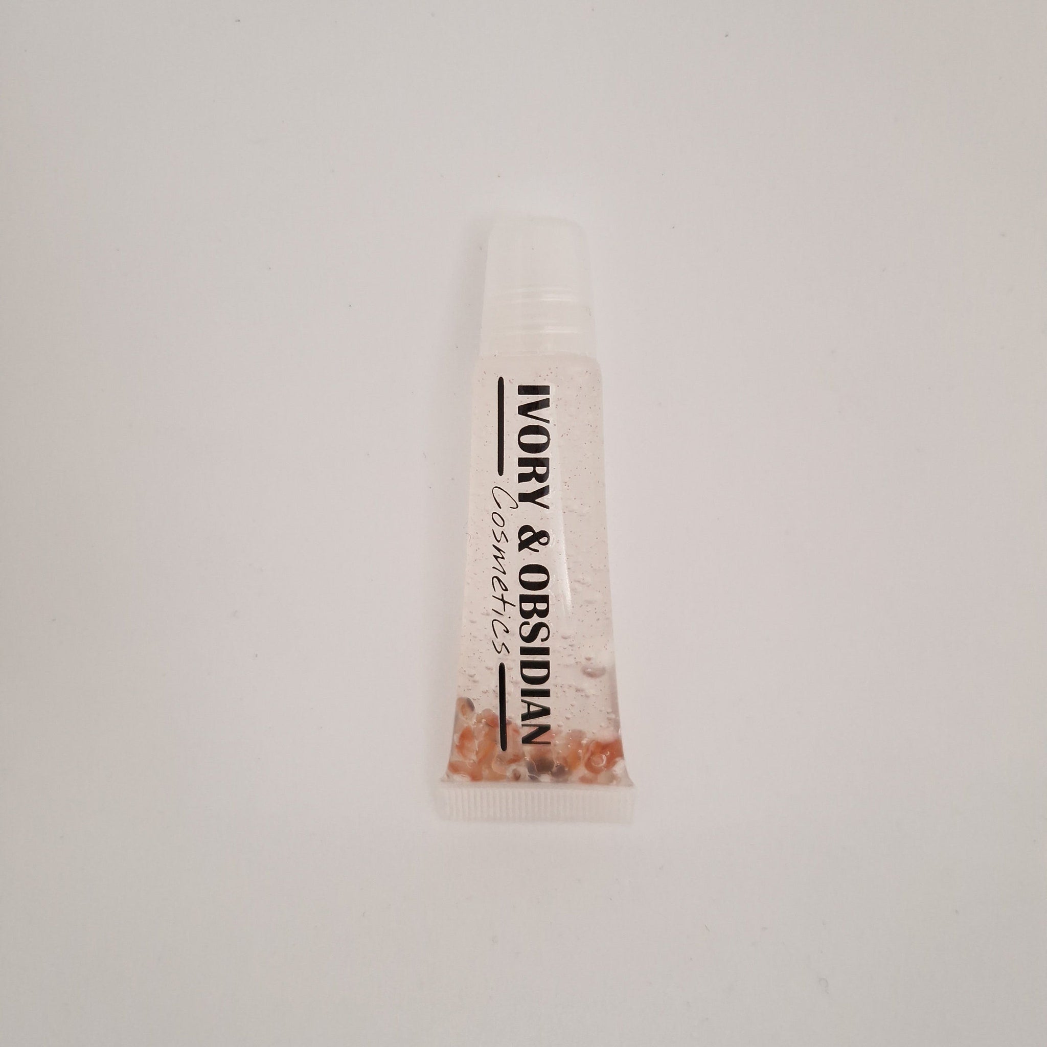 Lip gloss tube with clear liquid, Ivory & Obsidian branding, and small beads inside