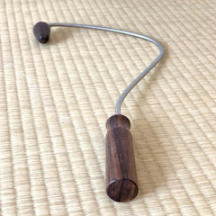 Manual tool with wood handle and curved metal arm, lying on a woven mat