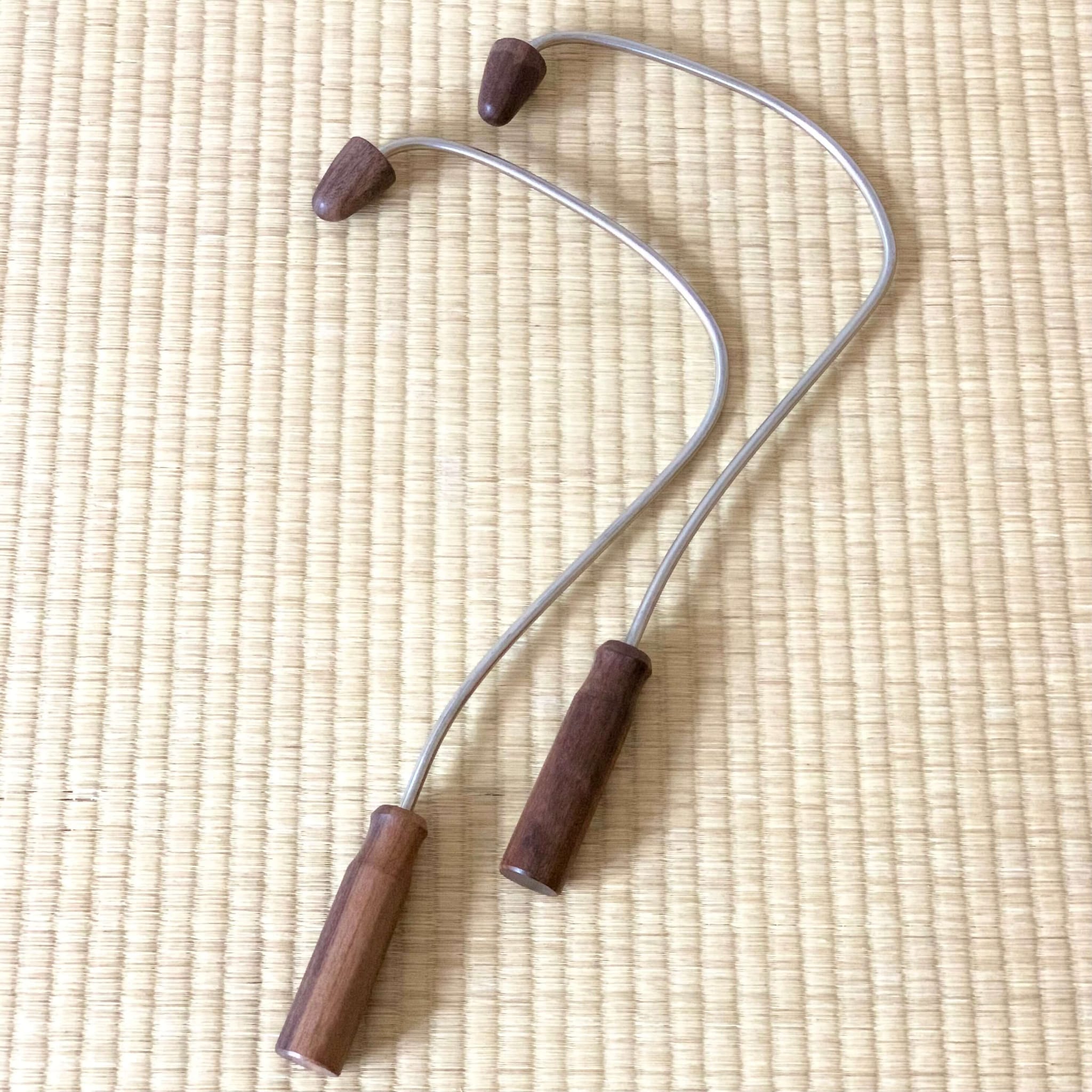 Massage tool with wooden handles and tips, silver metal frame, on woven mat background