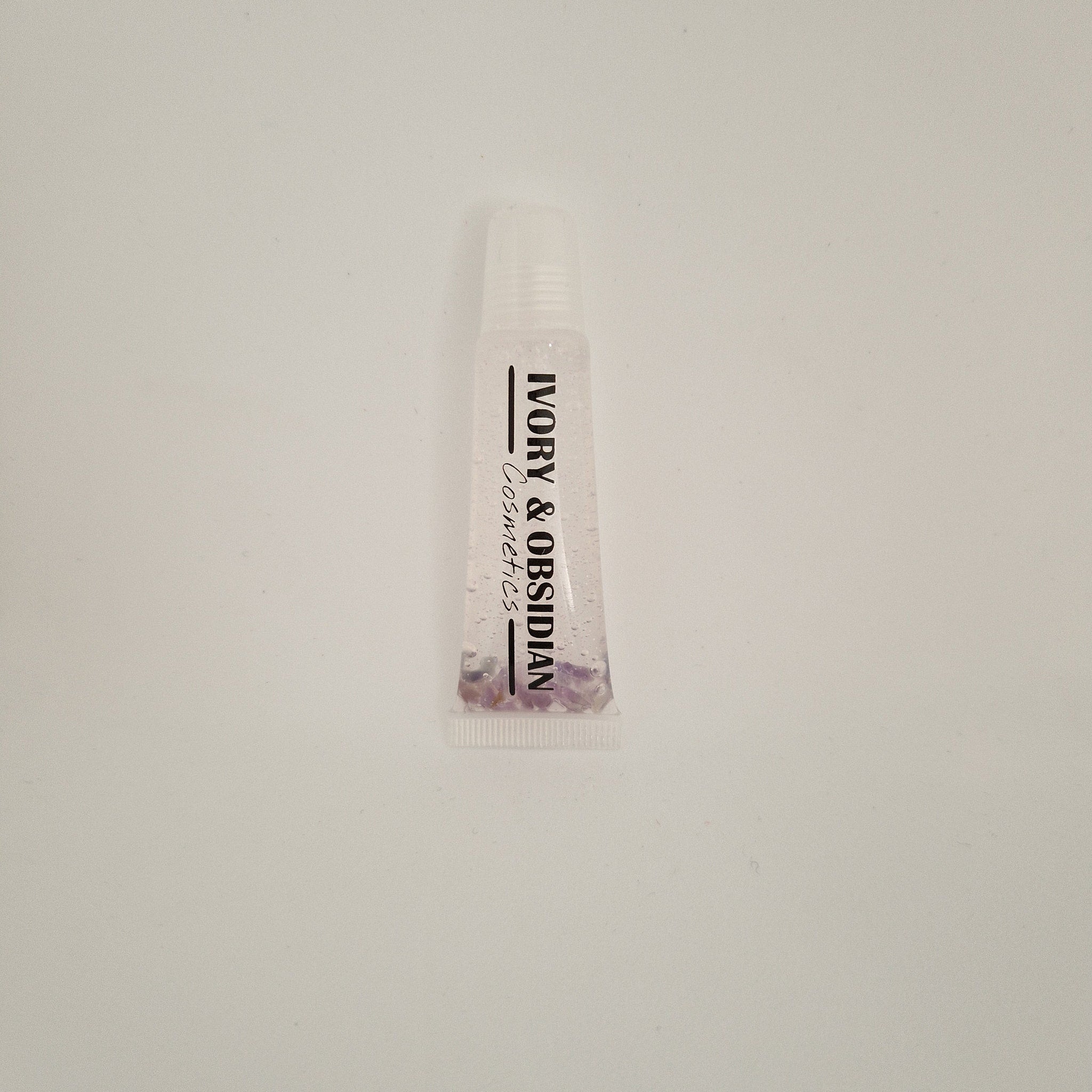Lip gloss tube with clear liquid, Ivory & Obsidian branding, and purple stones at the base
