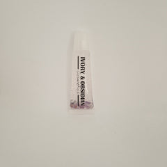 Lip gloss tube with clear liquid, Ivory & Obsidian branding, and purple stones at the base