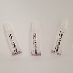 Lip gloss tubes with clear liquid, purple stones, and Ivory & Obsidian Cosmetics text on white background