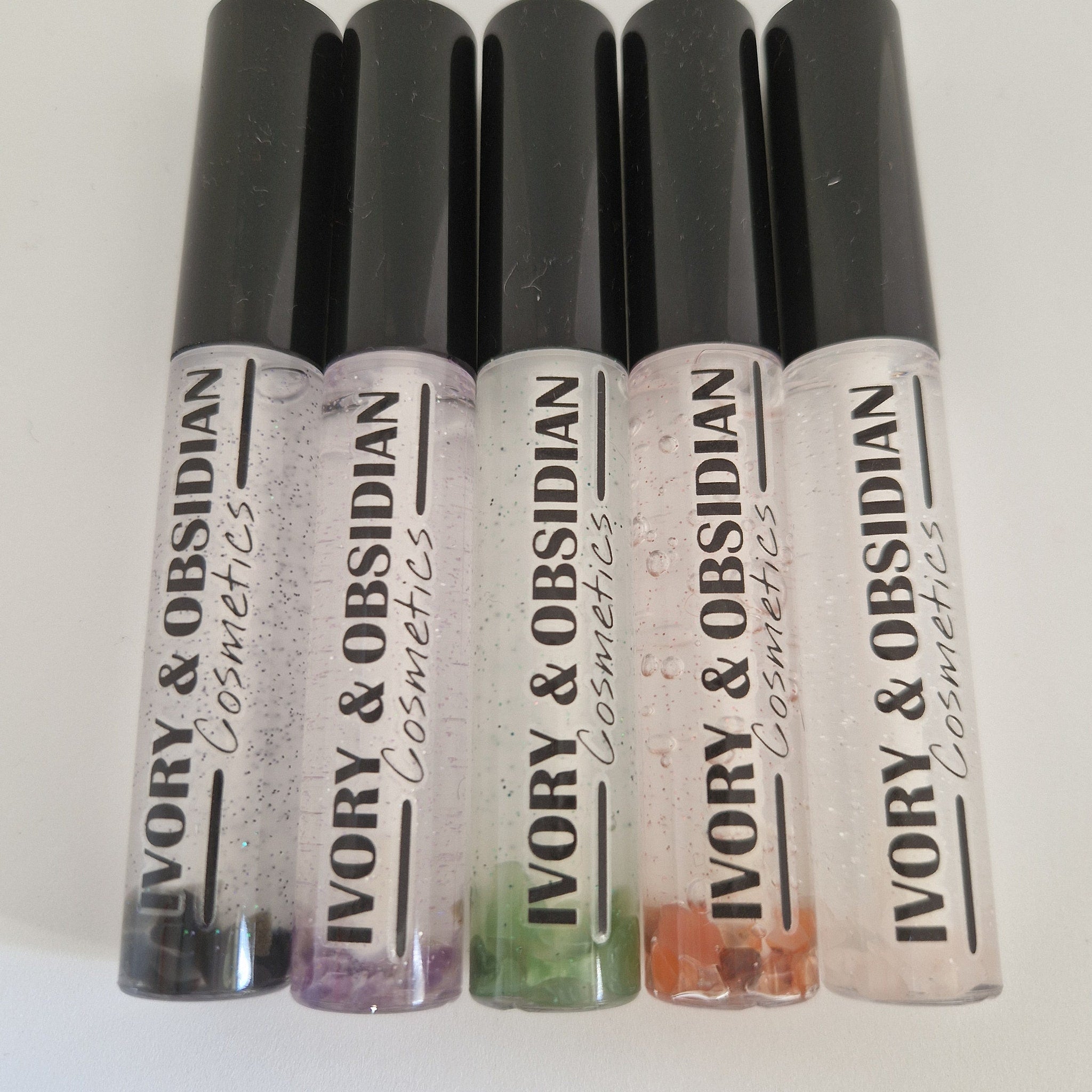 Lip gloss tubes with black caps, clear tubes, and IVORY & OBSIDIAN Cosmetics text visible